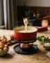 Kaasfondue in een rode fonduepan met stokbrood, krieltjes en broccoli om te dippen